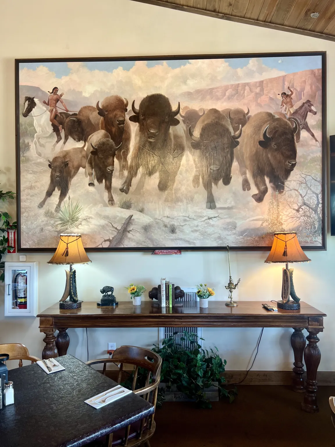 Large buffalo painting above wooden table setup.