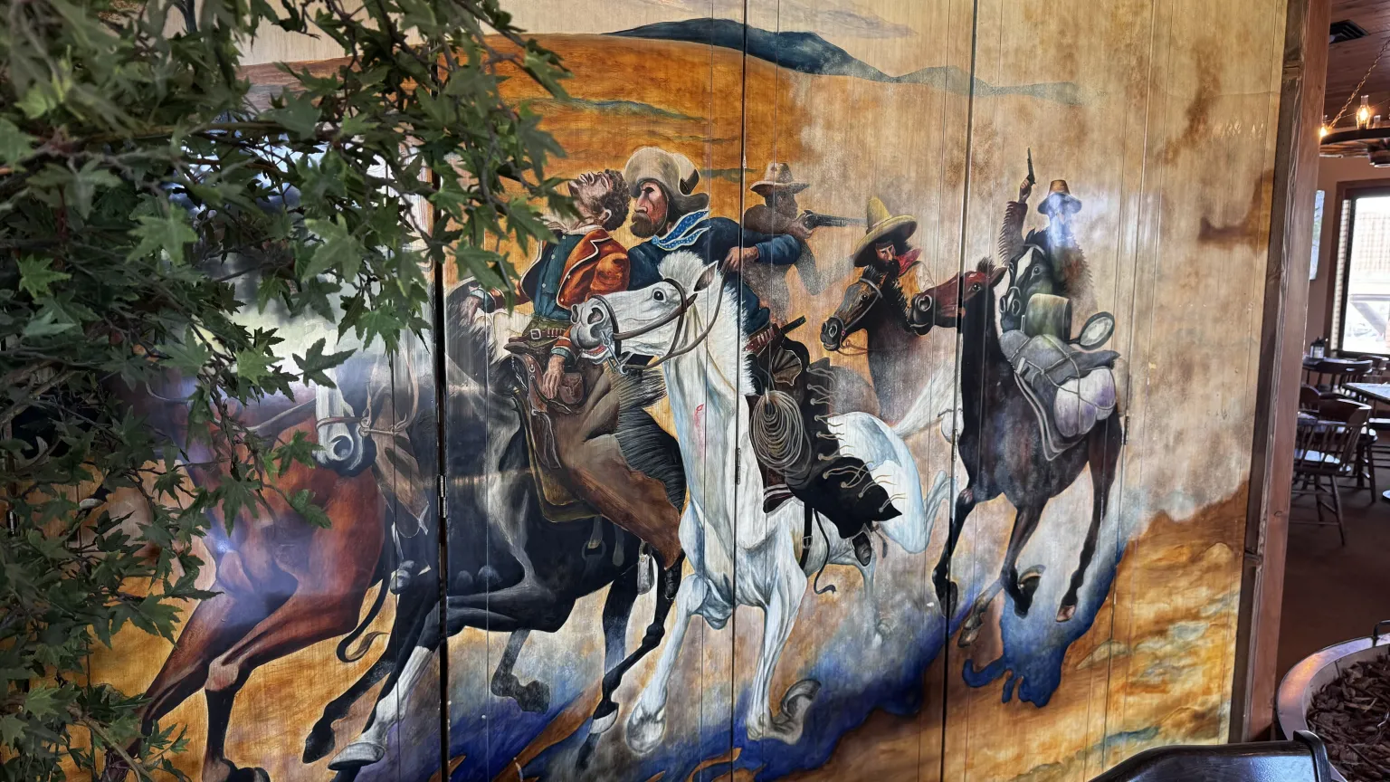 Cowboys riding horses in colorful mural.